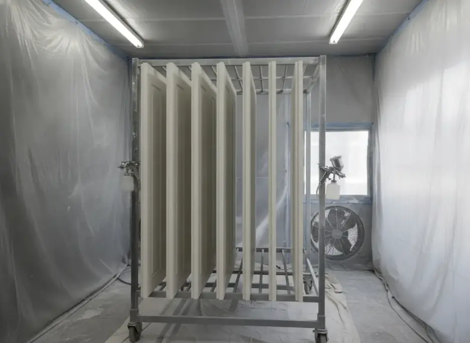 Cabinet doors in a satin off-white finish standing on a drying rack in a spray booth